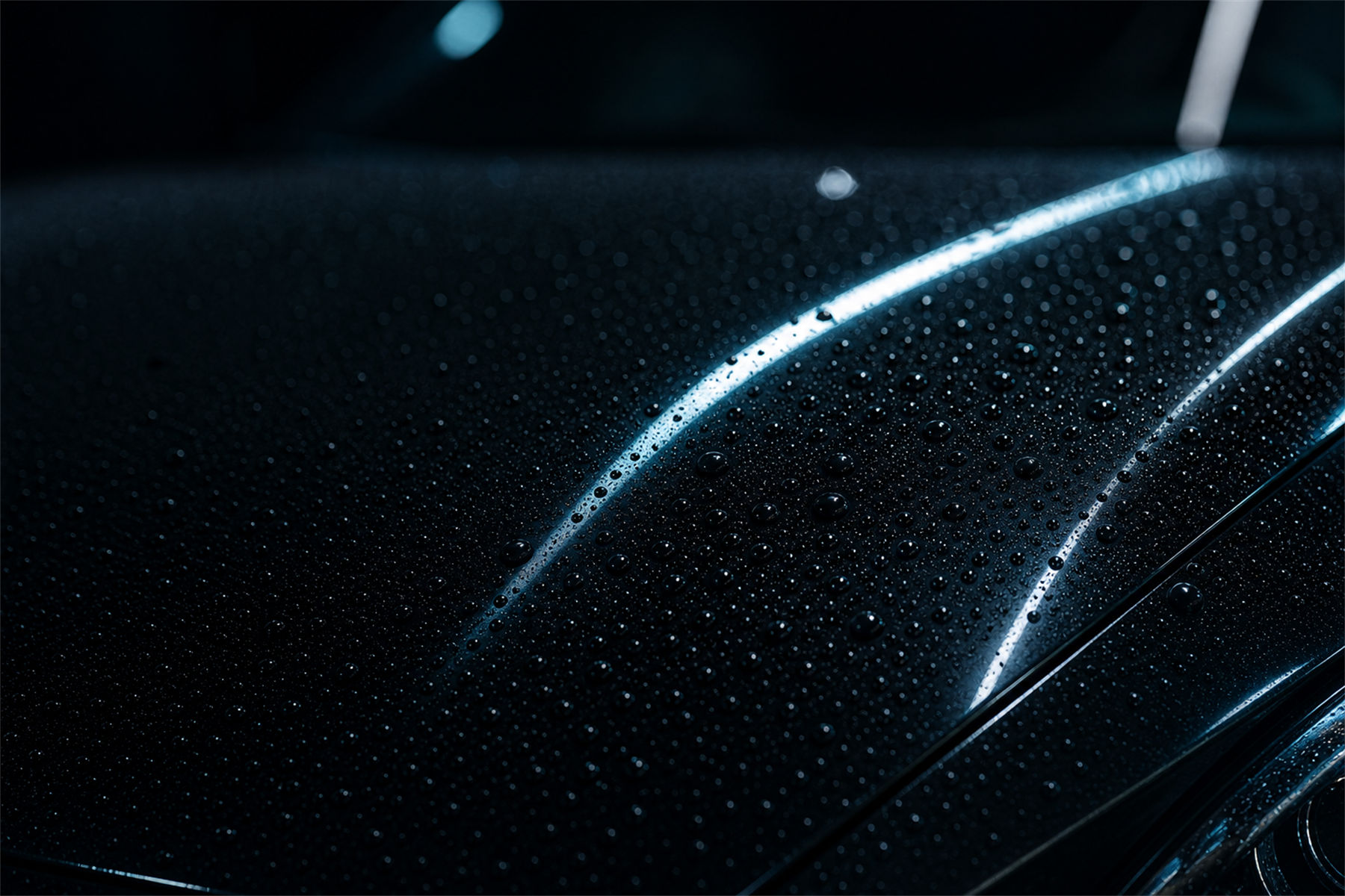 Frisch keramikversiegelte schwarze Motorhaube bei Nacht mit Wasser-Beading und cyanfarbenen Reflexen